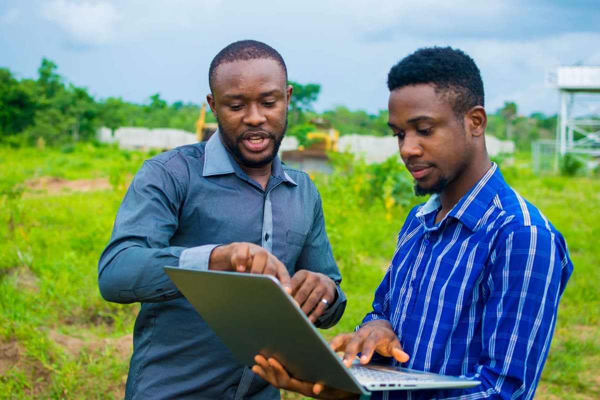 Two men looking through a laptop together outdoors